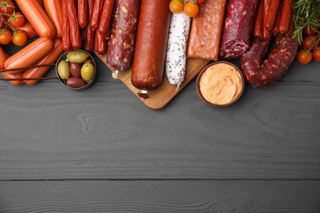 Different types of tasty sausages on gray wooden table, flat lay. Space for text