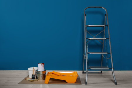 Metallic folding ladder and painting tools near blue wall indoors, space for textの写真素材