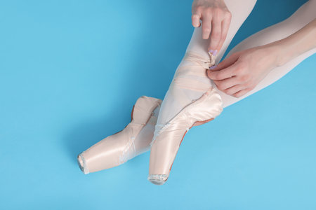 Young ballerina tying pointe shoes on light blue background, top viewの写真素材