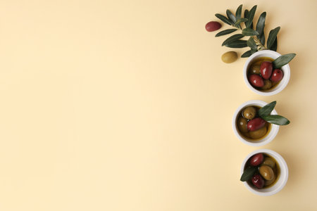 Bowls with different ripe olives and leaves on beige background, flat lay. Space for textの写真素材