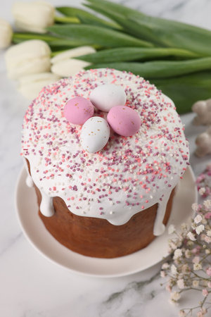 Tasty Easter cake with decorative sugar eggs and flowers on white marble table, above view