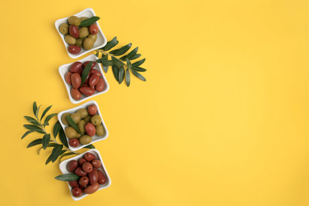 Different fresh olives and green leaves on yellow background, flat lay. Space for textの写真素材