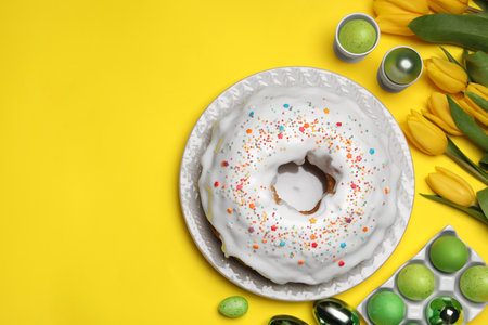 Easter cake with sprinkles, painted eggs and tulips on yellow background, flat lay. Space for textの写真素材