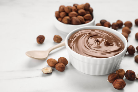 Bowl with chocolate paste and nuts on white marble table. Space for textの写真素材