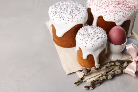 Tasty Easter cakes, decorated eggs and willow branches on gray table. Space for text