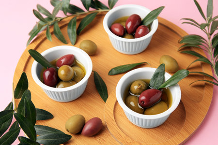 Wooden tray with different ripe olives and leaves on pink backgroundの写真素材