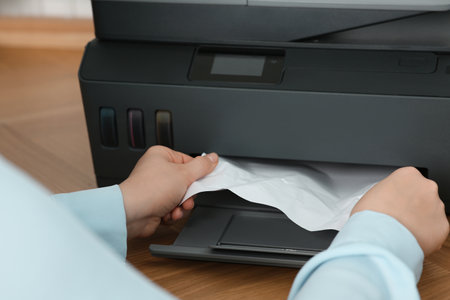 Woman taking crumpled paper out of printer at wooden table indoors, closeupの写真素材