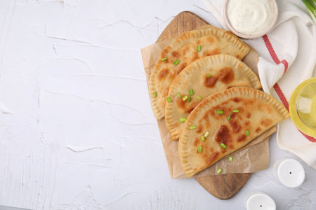 Delicious fried chebureki with cheese and green onion on white textured table, flat lay. Space for...