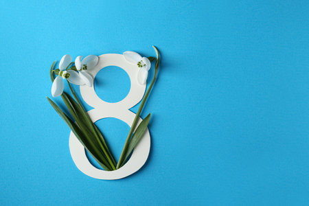 Beautiful snowdrops and paper number 8 on light blue background, flat lay. Space for text