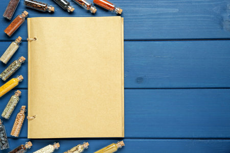 Blank recipe book and bottles with different spices on blue wooden table, flat lay. Space for textの写真素材