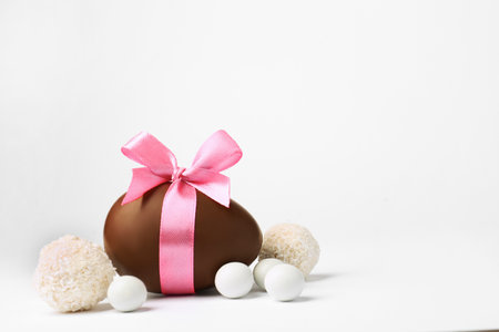 Sweet chocolate egg with pink bow and different candies on light background, space for textの写真素材