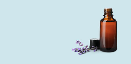 Bottle of lavender essential oil and flowers on pale light blue background, space for text. banner designの写真素材