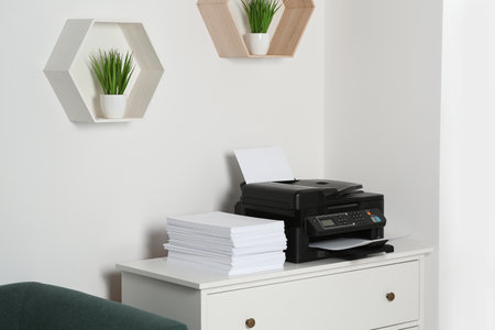 Modern printer and paper sheets on white chest of drawers indoorsの写真素材