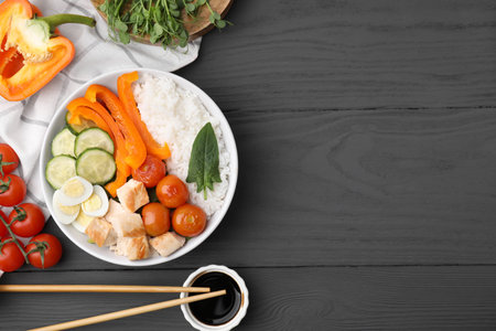 Delicious poke bowl with meat, rice, eggs and vegetables on black wooden table, flat lay. Space for textの写真素材