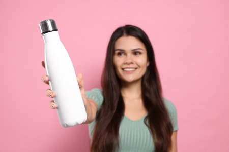 Young woman with thermo bottle against pink background, focus on handの写真素材