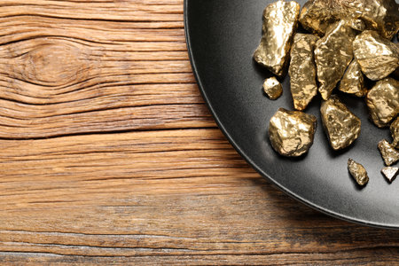 Plate of gold nuggets on wooden table, top view. Space for textの写真素材