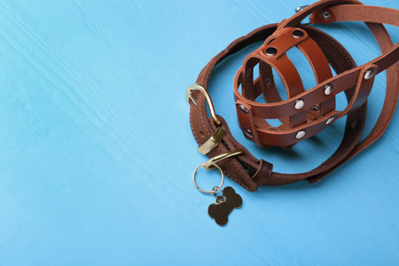 Brown leather dog muzzle and collar on light blue wooden table. Space for textの写真素材