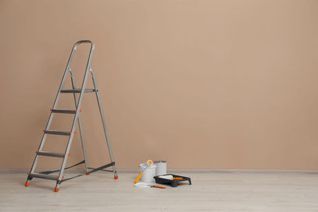Metallic folding ladder and painting tools near beige wall indoors, space for textの写真素材
