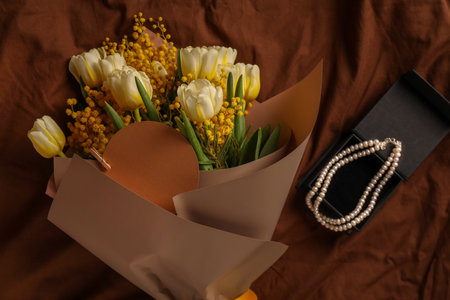 Bouquet of beautiful spring flowers, blank card and necklace on brown fabric, flat layの写真素材