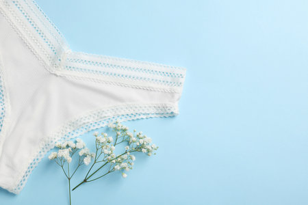 White women's underwear and flowers on light blue background, flat lay. Space for text