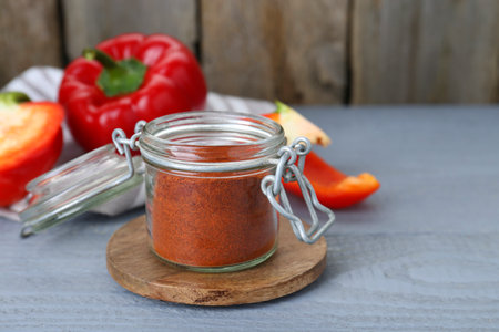 Jar with aromatic paprika powder and fresh bell peppers on gray wooden tableの写真素材