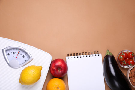 Scales, notebook, fresh fruits and vegetables on light brown background, flat lay with space for text. Low glycemic index dietの写真素材