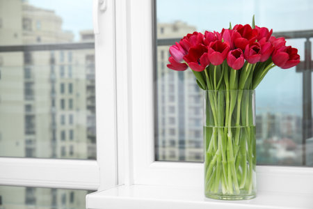 Bouquet of beautiful tulips in glass vase on window sill indoors. Space for textの写真素材