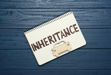 Notebook with word Inheritance and model of car on blue wooden background, top view