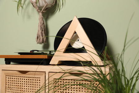 Vinyl records and player on wooden cabinet near light green wall