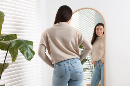 Young woman in stylish jeans near mirror indoorsの写真素材