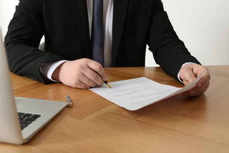Notary signing document on wooden table, closeup