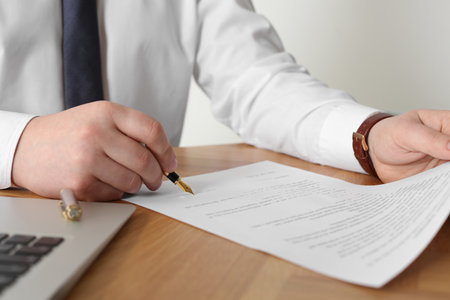 Notary signing document on wooden table, closeup