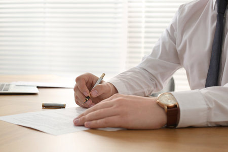 Notary signing document at wooden table in office, closeup