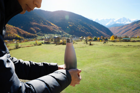 Boy holding thermo bottle with drink in mountains on sunny day, closeupの写真素材