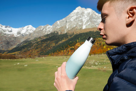 Boy drinking from thermo bottle in mountains on sunny day. Space for textの写真素材