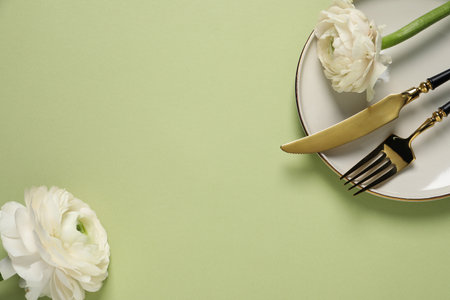 Stylish table setting with cutlery and flowers on light green background, flat lay. Space for text