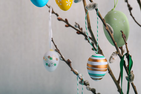 Closeup view of beautiful willow branches with painted eggs on light blue gray background, space for text. Easter decorの写真素材