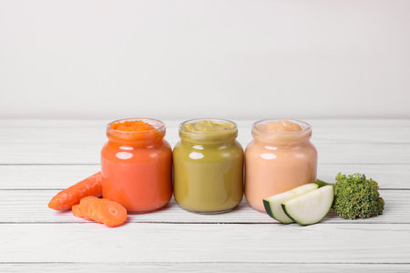 Jars of healthy baby food and vegetables on white wooden tableの写真素材