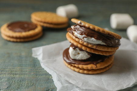 Delicious marshmallow sandwiches with crackers and chocolate on light blue wooden table, closeup....