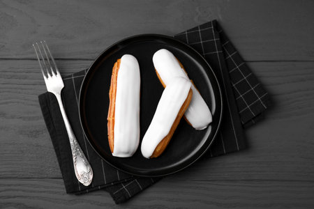 Delicious eclairs covered with glaze on gray wooden table, top view