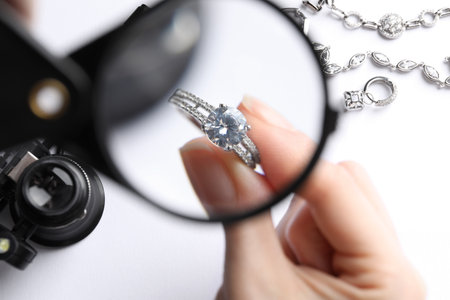 Jeweler examining diamond ring with magnifying glass at white table, closeupの写真素材