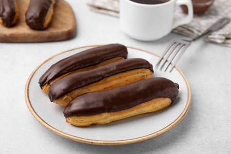 Delicious eclairs covered with chocolate on gray table