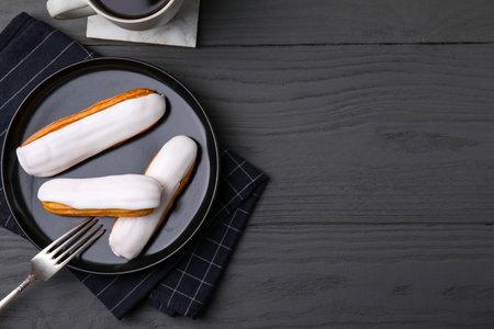 Delicious eclairs covered with glaze on gray wooden table, flat lay. Space for textの写真素材