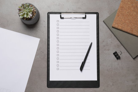 Clipboard with checkboxes, plant and office stationery on gray table, flat lay. Checklist