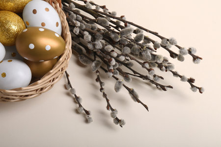 Wicker basket with decorated Easter eggs and willow branches on beige background, closeupの写真素材