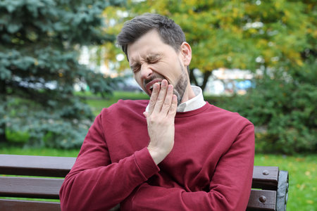 Sleepy tired man yawning on bench in beautiful green park
