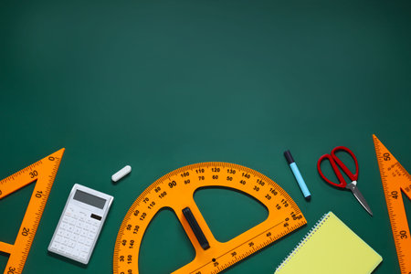 Flat lay composition with protractor, triangle and stationery on green chalkboard. Space for text