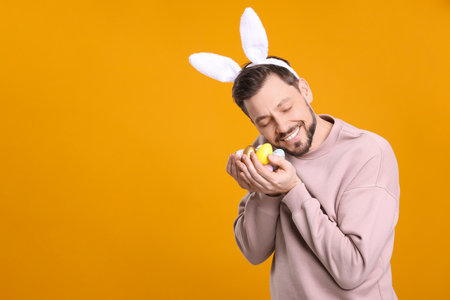 Happy man in bunny ears headband holding painted Easter eggs on orange background. Space for textの写真素材