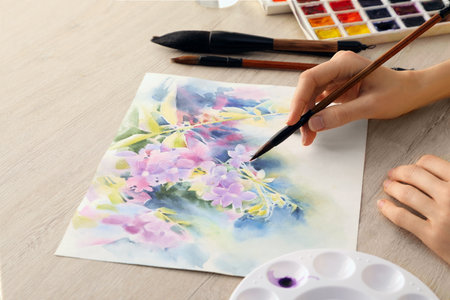 Woman painting flowers with watercolor on white wooden table, closeup. Creative artworkの写真素材