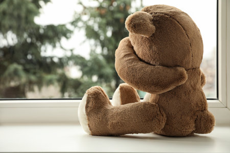 Cute lonely teddy bear on windowsill indoors. Space for textの写真素材